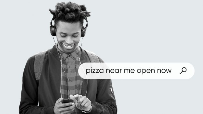 ヘッドフォンをつけ、携帯電話を使用して現在営業中の「近くのピザ屋」を検索する男性